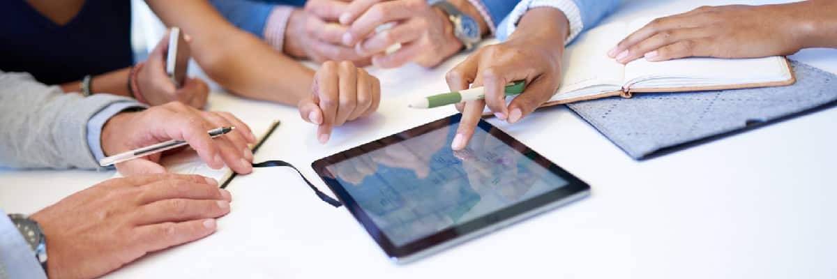 Group of Hands On a Table Discussing Data On a Tablet
