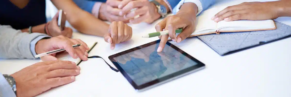 Group of Hands On a Table Discussing Data On a Tablet