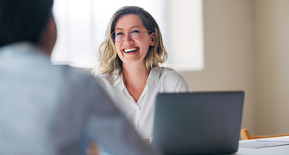 Image shows a professional woman smiling beside her laptop.